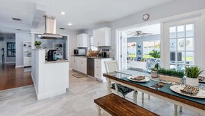 Una cocina moderna con armarios blancos, una isla central y una zona de comedor con banco.