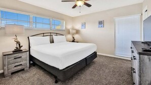 Une chambre à coucher comprenant un lit, un ventilateur de plafond, des lampes de chevet, une table de chevet et une commode.