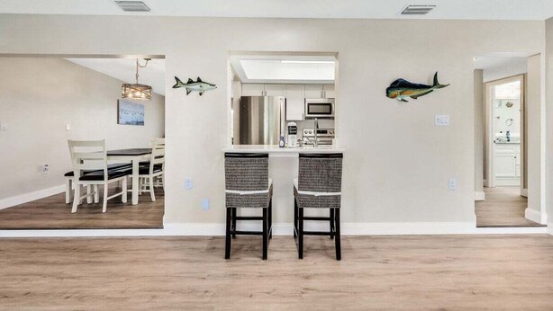 Une cuisine moderne dotée d’appareils électroménagers en acier inoxydable, un coin repas avec deux chaises en osier et des décorations murales représentant des poissons.