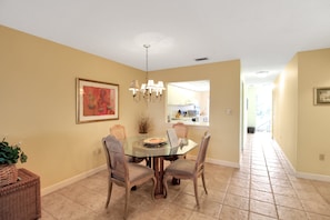 A dining area with a glass table, wicker chairs, a chandelier, and a framed artwork on the wall.