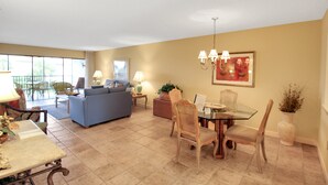 A spacious living area with a blue sofa, dining table, and chairs, a balcony with outdoor seating, and a large window providing natural light. - Breathtaking beach views await from this 2BR 2nd floor condo on Longboat Key The Beach Fact Oar (Longboat Key)