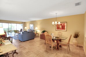 A spacious living area with a blue sofa, dining table, and chairs, a balcony with outdoor seating, and a large window providing natural light. - Breathtaking beach views await from this 2BR 2nd floor condo on Longboat Key The Beach Fact Oar (Longboat Key)