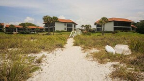 En sti der fører til en række moderne huse med røde tage, omgivet af grønne arealer og sand.