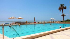 Una piscina con lettini e ombrelloni, una palma e vista libera sull'oceano.