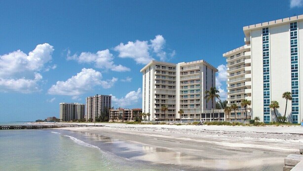 Een hotel aan het strand met meerdere hoge gebouwen, een zandstrand en een helderblauwe lucht.