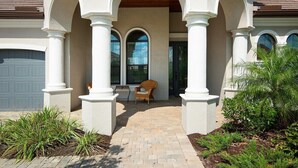 A house with a covered porch, white columns, and a brick pathway leading to a door. - Gorgeous lakefront pool home with golf course view Birdie (Lakewood Ranch)
