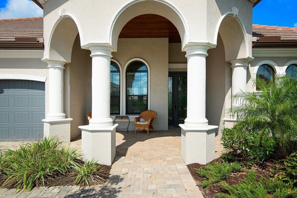 A house with a covered porch, white columns, and a brick pathway leading to a door. - Gorgeous lakefront pool home with golf course view Birdie (Lakewood Ranch)
