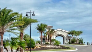 A building with an arched entrance, surrounded by palm trees and a landscaped garden. - Gorgeous lakefront pool home with golf course view Birdie (Lakewood Ranch)