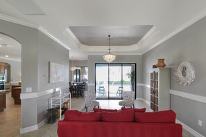 A spacious living area with a red sofa, a chandelier, and a view to an outdoor patio.