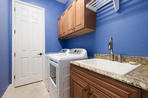 A laundry room with a white washing machine, a sink, and wooden cabinets. - Gorgeous lakefront pool home with golf course view Birdie (Lakewood Ranch)