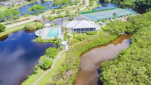 Vue aérienne d’un complexe hôtelier doté de plusieurs piscines, d’un grand bâtiment à la façade en verre et d’un environnement verdoyant.