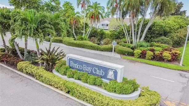 Une enseigne indiquant l’emplacement du Peninsula Bay Club, avec un espace paysager agrémenté de palmiers et d’arbustes.