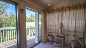 Une pièce dotée d’une porte vitrée donnant sur un balcon, d’une table ronde avec des chaises, d’une lampe et d’une horloge murale.