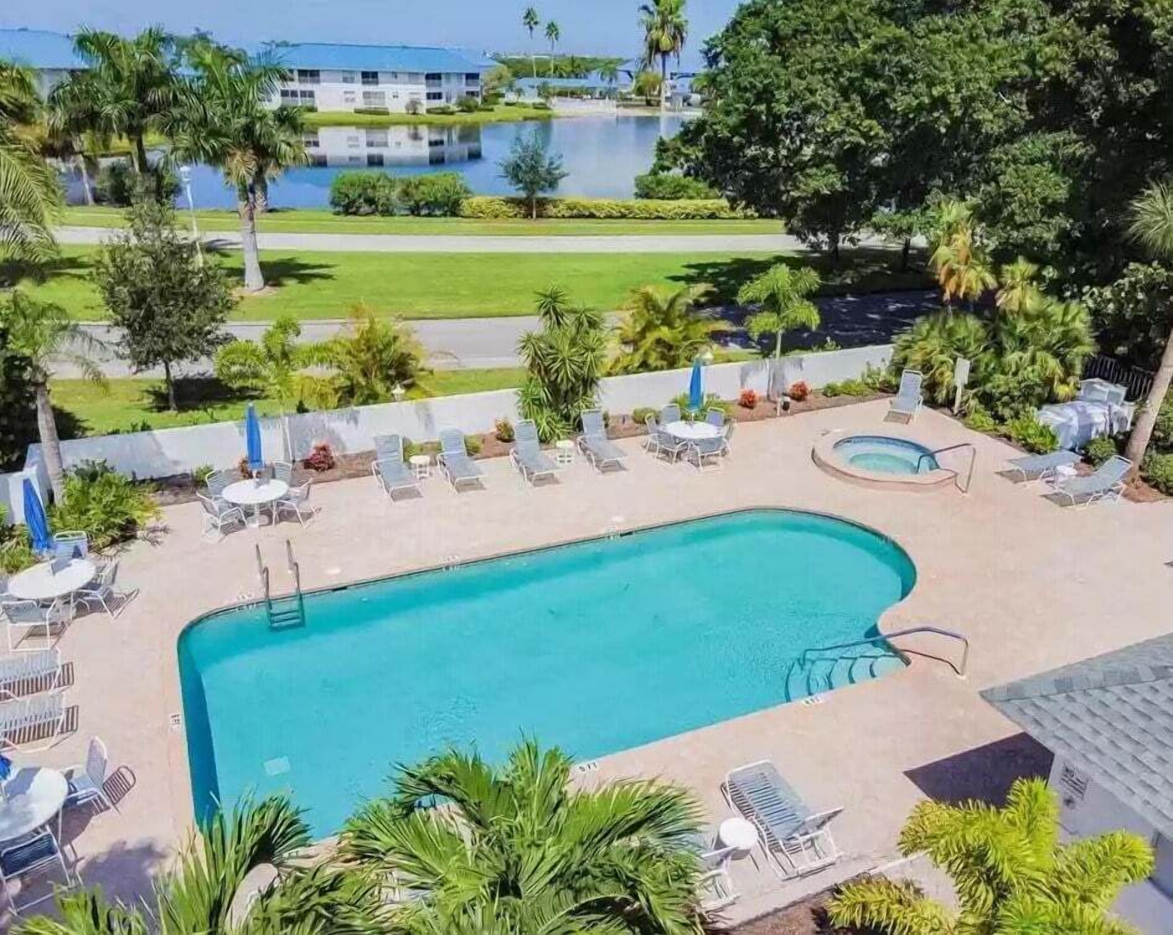 En pool med solstolar och parasoller, omgiven av grönska och med en byggnad synlig i bakgrunden.