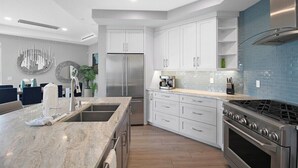A modern kitchen with white cabinets, a stainless steel refrigerator, a gas stove, and a blue-tiled backsplash. - Luxury 4BR Siesta Key villa - Walk to the beach - Beach House Residences Unit 1 (Sarasota)