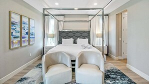 A modern bedroom with a large bed, two armchairs, a ceiling fan, and artwork on the wall. - Luxury 4BR Siesta Key villa - Walk to the beach - Beach House Residences Unit 1 (Sarasota)