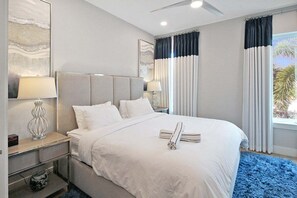 A hotel room with a large bed, two bedside tables with lamps, a ceiling fan, and a view of palm trees through the window. - Luxury 4BR Siesta Key villa - Walk to the beach - Beach House Residences Unit 1 (Sarasota)