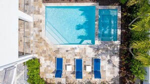An aerial view of a swimming pool with two separate sections, surrounded by a stone deck and lush greenery. - Luxury 4BR Siesta Key villa - Walk to the beach - Beach House Residences Unit 1 (Sarasota)