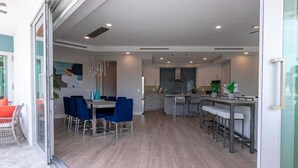A modern kitchen with a central island, a dining area with blue chairs, and a glass door leading to an outdoor space. - Luxury 4BR Siesta Key villa - Walk to the beach - Beach House Residences Unit 1 (Sarasota)
