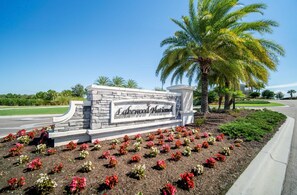 A sign with 'Lakewood National' written on it, surrounded by a landscaped area with flowers and palm trees. - Lakefront 2 BR/2 BA condo in Lakewood National Golf Club - Pearl in the Rough (Bradenton)