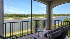 A balcony with a view of a lake and golf course, furnished with wicker chairs and a small table. - Lakefront 2 BR/2 BA condo in Lakewood National Golf Club - Pearl in the Rough (Bradenton)