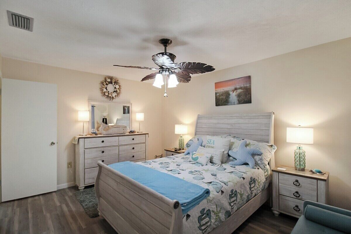 A bedroom with a bed, nightstands, a ceiling fan, a dresser, and a door.