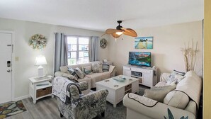 A cozy living room with a sofa, armchairs, a coffee table, a TV, and a ceiling fan.