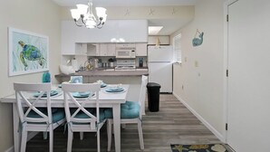 A modern kitchen with white cabinets, a microwave, and a refrigerator. There is a dining table with chairs and a chandelier above.