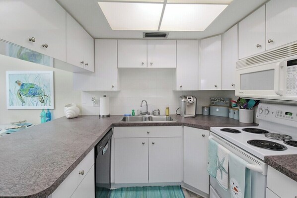 Une cuisine moderne avec des meubles blancs, un plan de travail en granit, un four à micro-ondes et une cuisinière.