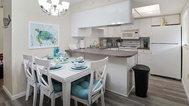 A modern kitchen with white cabinets, a central island, and a dining area with white chairs.