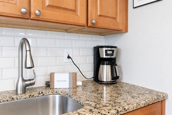 A kitchen with a stainless steel sink, a modern faucet, a coffee maker, and wooden cabinets.