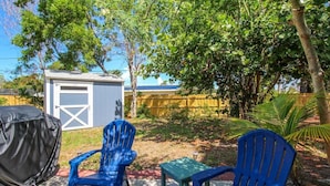 A backyard with two blue chairs, a small table, and a covered grill. - Charming home near Manasota Key Beach Beach Heron (Venice)
