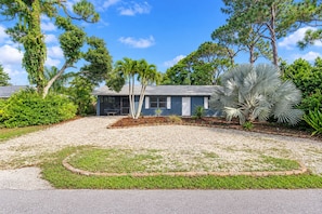 A modern two-story house with a gravel driveway, surrounded by a variety of trees and shrubs.