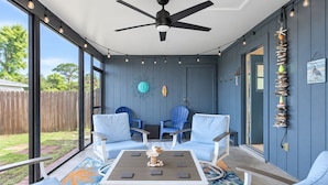 A room with a ceiling fan, two blue chairs, a table with decorative items, and a view of the outdoors. - Charming home near Manasota Key Beach Beach Heron (Venice)