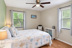 Un dormitorio con cama, mesita de noche, lámpara, silla, escritorio, computadora y ventilador de techo.