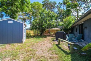 A backyard with a wooden deck, a barbecue grill, and a covered seating area with chairs.
