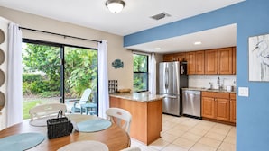 A modern kitchen with stainless steel appliances, wooden cabinets, and a dining area with a view of the garden. - Charming home near Manasota Key Beach Beach Heron (Venice)