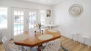 A dining area with a wooden table, white chairs, and a view of a pool through the glass doors. - Bright and cozy pool home in Sarasota - Bali Poolside (Sarasota)