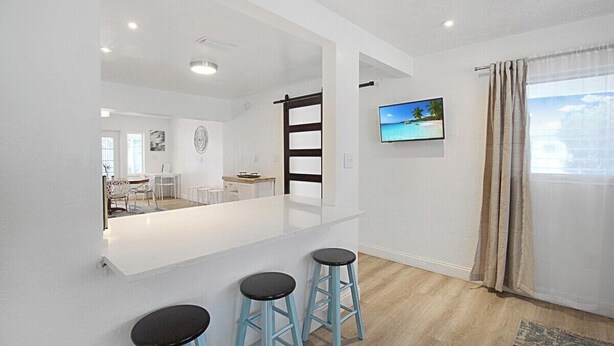 A modern kitchen with a white island, blue bar stools, and a TV mounted on the wall. - Bright and cozy pool home in Sarasota - Bali Poolside (Sarasota)