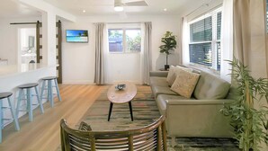 A living room with a sofa, a coffee table, a TV, and a window with curtains. - Bright and cozy pool home in Sarasota - Bali Poolside (Sarasota)