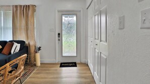 A hallway with a dark-colored sofa, a wicker chair, a doormat, and a door with frosted glass. - Bright and cozy pool home in Sarasota - Bali Poolside (Sarasota)