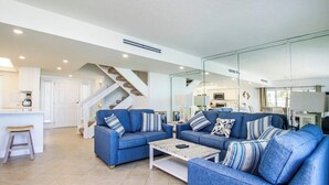 Una sala de estar moderna con sofás azules, una mesa de centro y una escalera que lleva a la cocina.