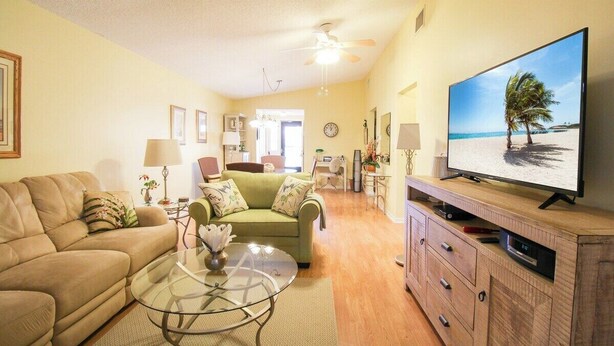 Een woonkamer met een beige bank, een groene fauteuil, een glazen salontafel en een televisie op een houten dressoir.