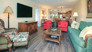 Ein Wohnzimmer mit Fernseher, roten Sesseln, einem grünen Sofa und einem Holzkabinett.
