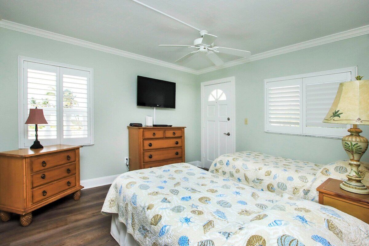 A bedroom with two beds, a ceiling fan, a TV, a dresser, and a lamp.