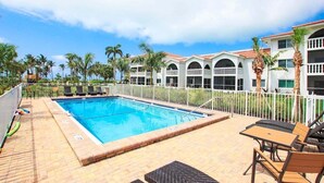Ein Swimmingpool mit weißem Zaun, Liegestühlen und Palmen.