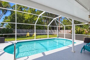 Une piscine couverte, surmontée d’une structure de toit blanche, entourée d’une clôture en bois et de verdure.