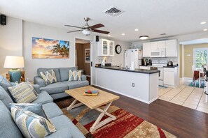 A modern living room with a sofa, coffee table, and a painting of a sunset. - 3 BR Pool Home In Nokomis - Close To Beaches - Tropical Escape (Nokomis)