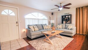 A living room with a grey sofa, wooden coffee table, and a ceiling fan. - 3 BR Pool Home In Nokomis - Close To Beaches - Tropical Escape (Nokomis)