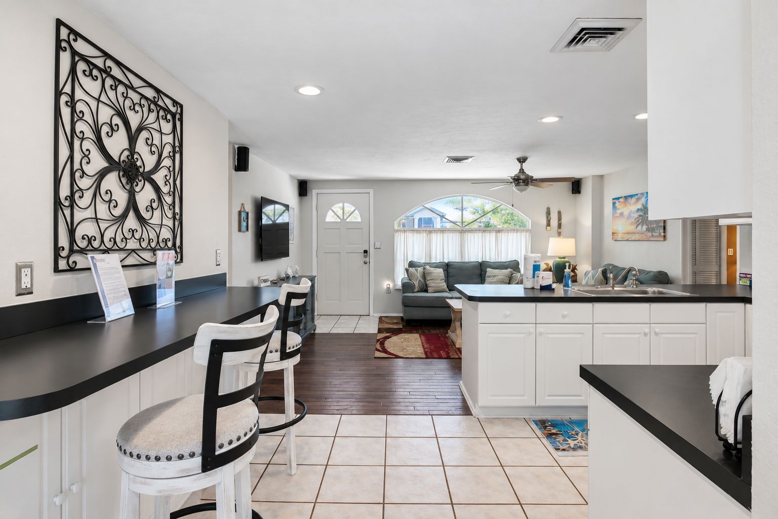 A modern kitchen with a bar area, white cabinetry, and a dining space with a grey sofa.